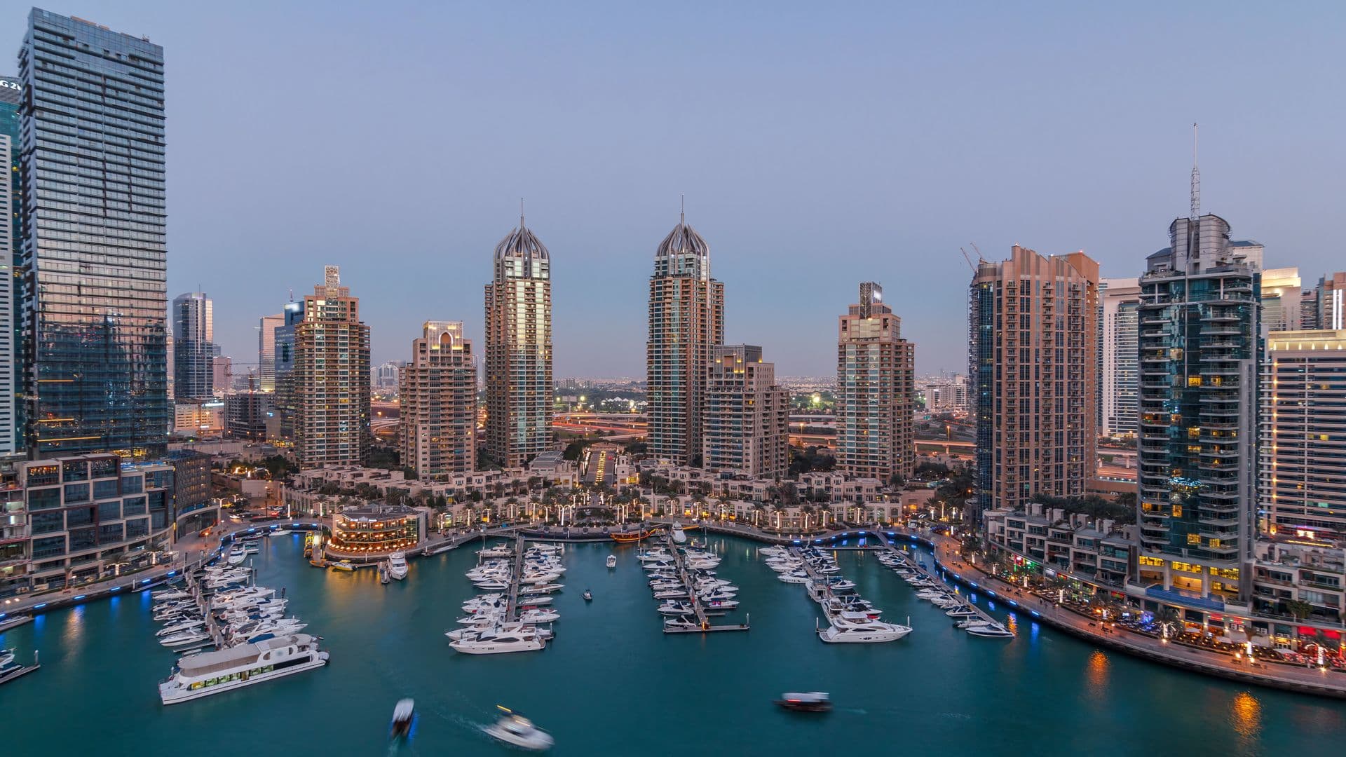 Dubai Marina at dusk, with yachts moored in the marina and lit residential towers along the waterfront