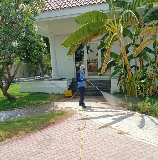 Star Al Madina technician in uniform and face mask spraying a residual treatment along the paved edge of a Dubai villa garden