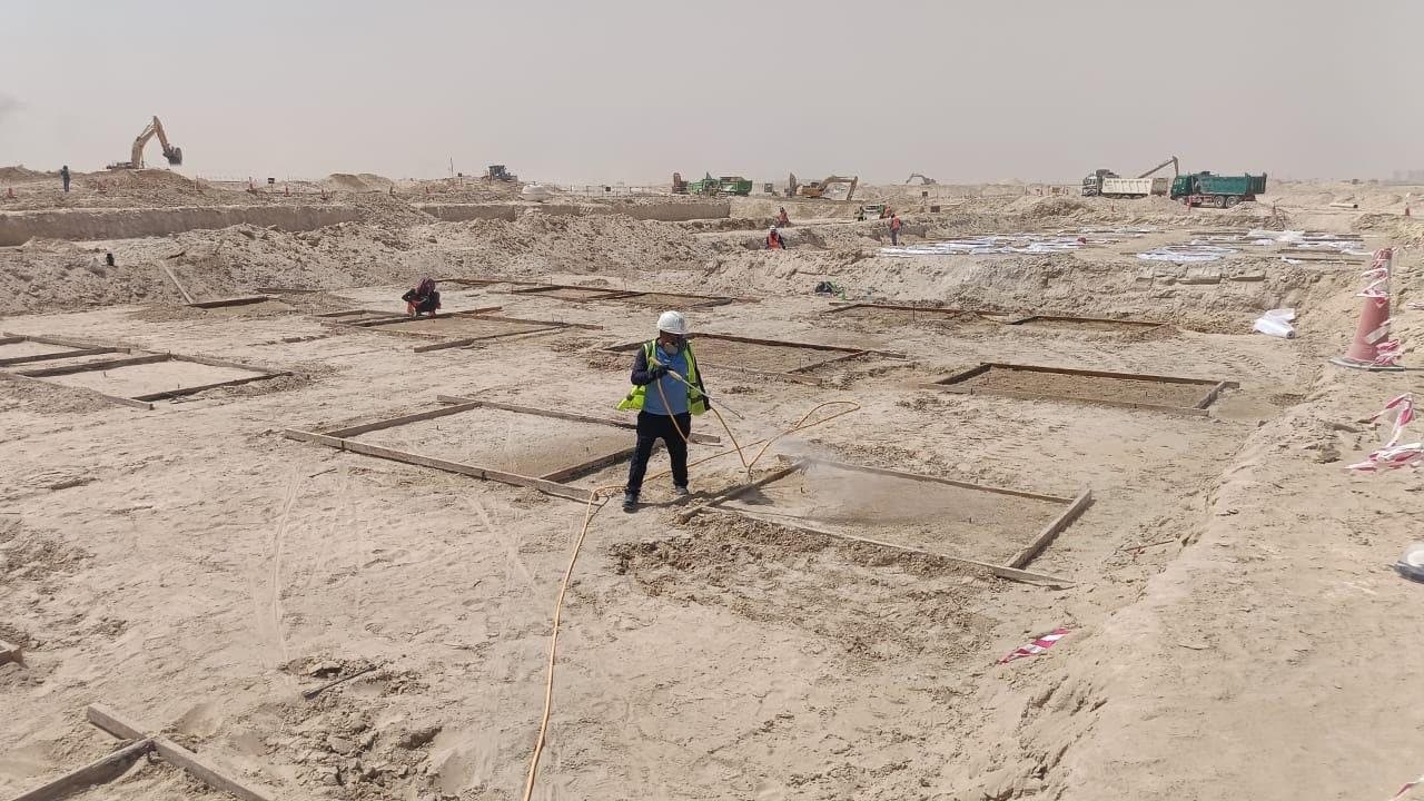 Star Al Madina technician in hi-vis and respirator spraying termiticide into timber-formed footing excavations across a Dubai construction site, with excavators and tipper trucks working behind